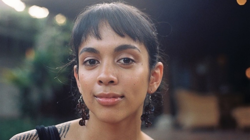 a woman smiles looking directly at the camera, she has dangly black earings on.