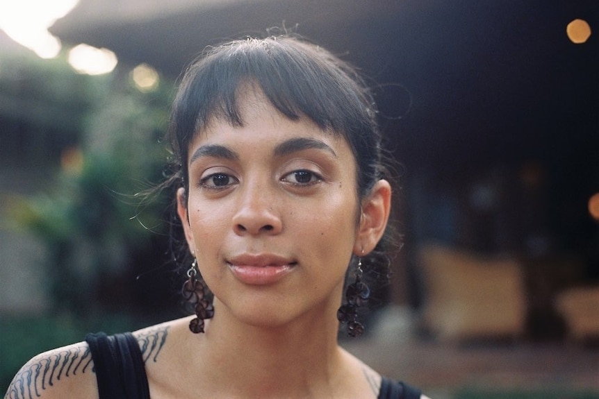A woman smiles looking directly at the camera, she has dangly black earings on.