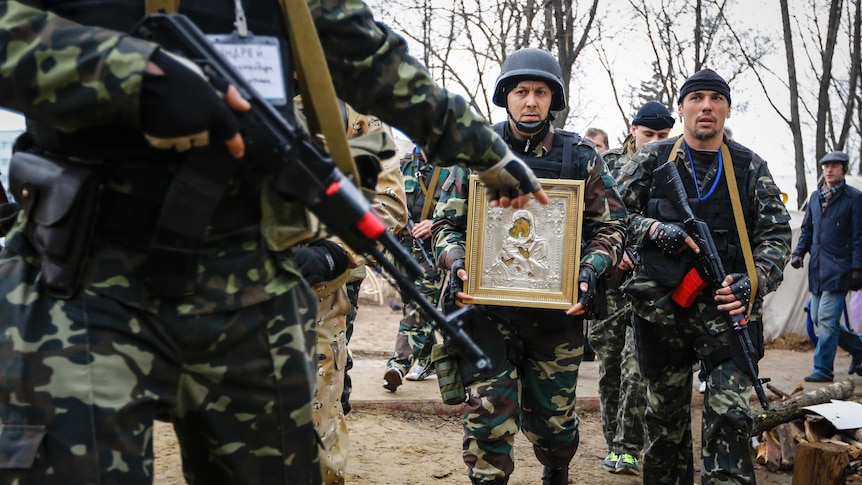 Armed pro-Russian protesters escort a comrade who is carrying an icon