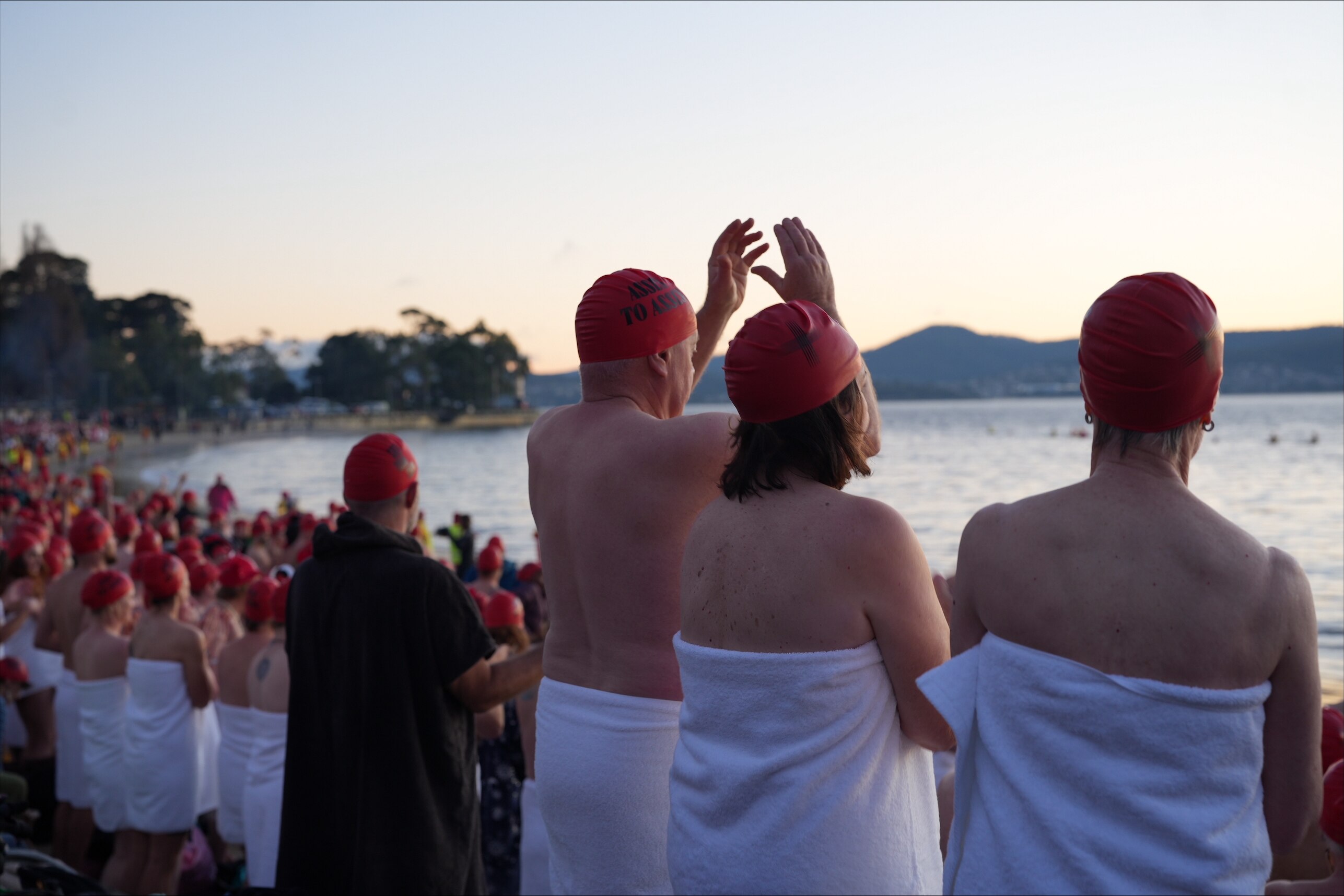 Groups of swimmers wearing towels prepare to enter the water for Dark Mofo's 2026 Nude Solstice Swim