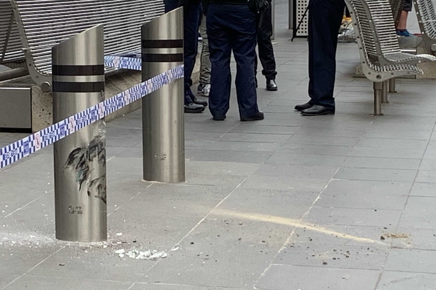 A blue and white strip of police tape is wrapped around steel bollards at a CBD open pedestrian mall.
