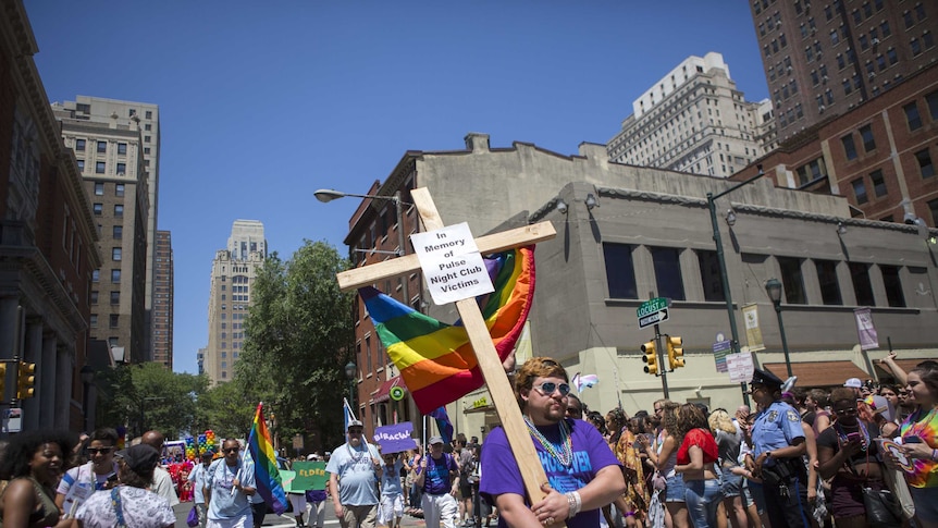 Man carries a cross with a sign in memory of the victims of the Pulse nightclub shooting