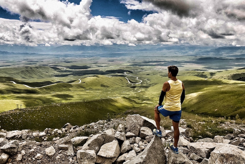 Man dresses in running clothes stands in a high vantage point looking at the view.