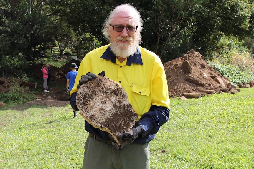 Man with beard and high-vis shirt holds a piece of headstone covered in dirt
