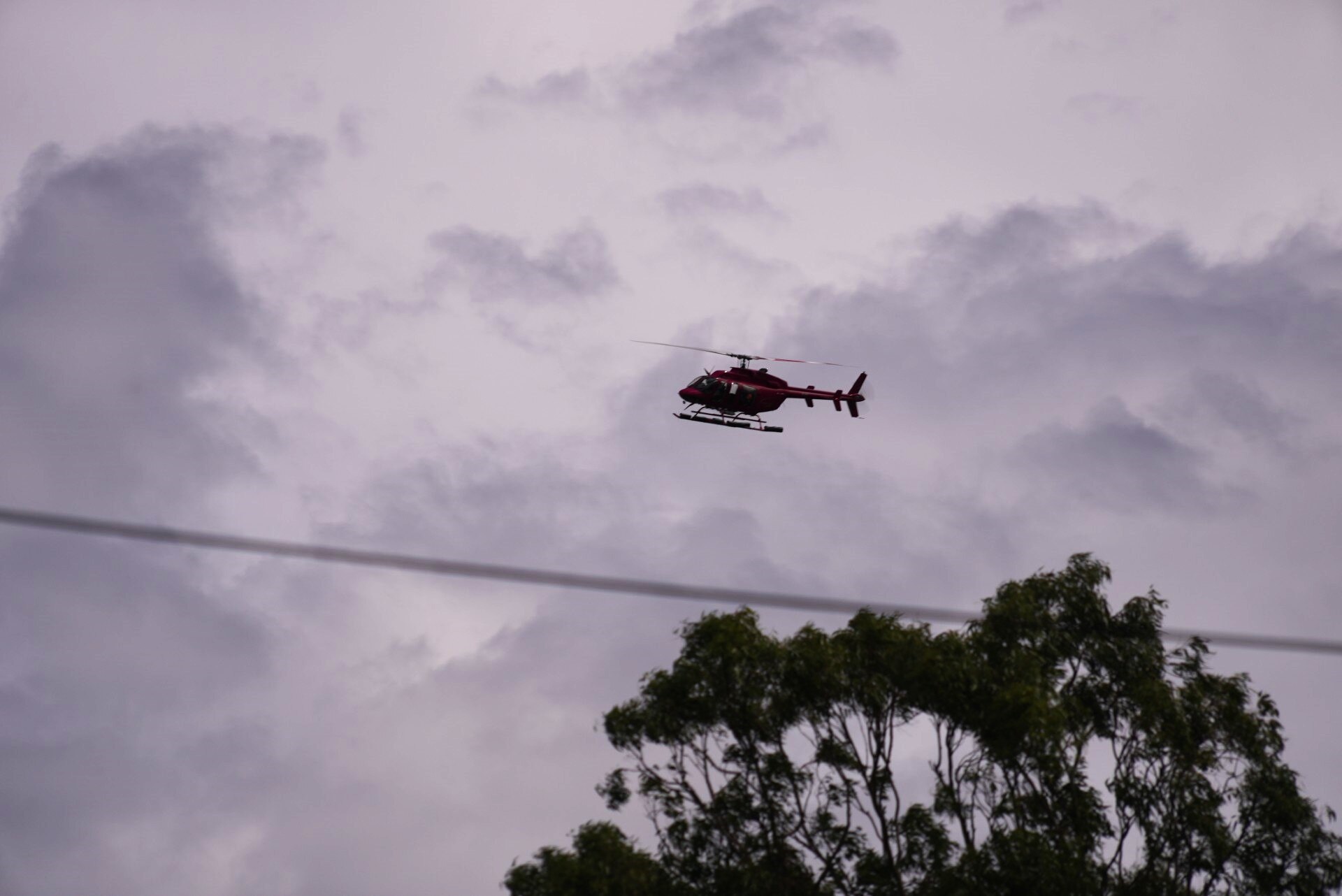 A red helicopter takes off under grey skies.