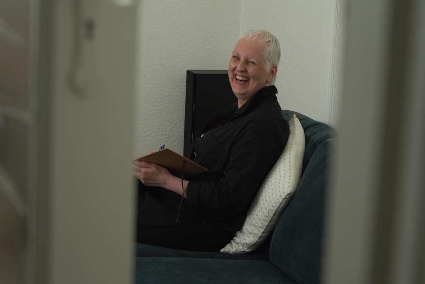 A woman sitting on a sofa, laughing at the camera.