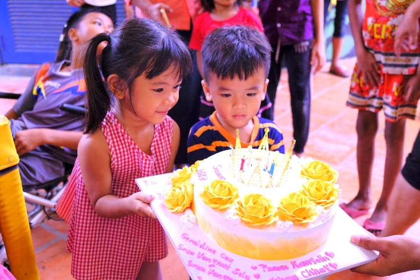A girl and a boy look at a birthday cake with yellow decorations