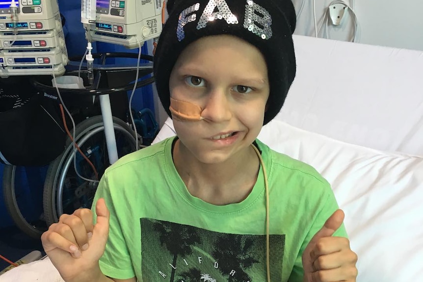 A young boy wearing beanie that says FAB gives two thumbs up. He is smiling on one side of his face.