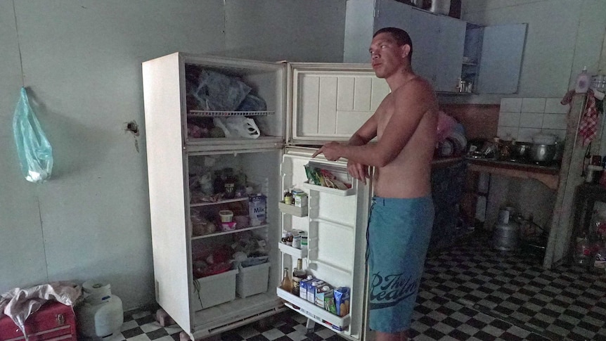 Man stands next to his open fridge pointing at food inside.