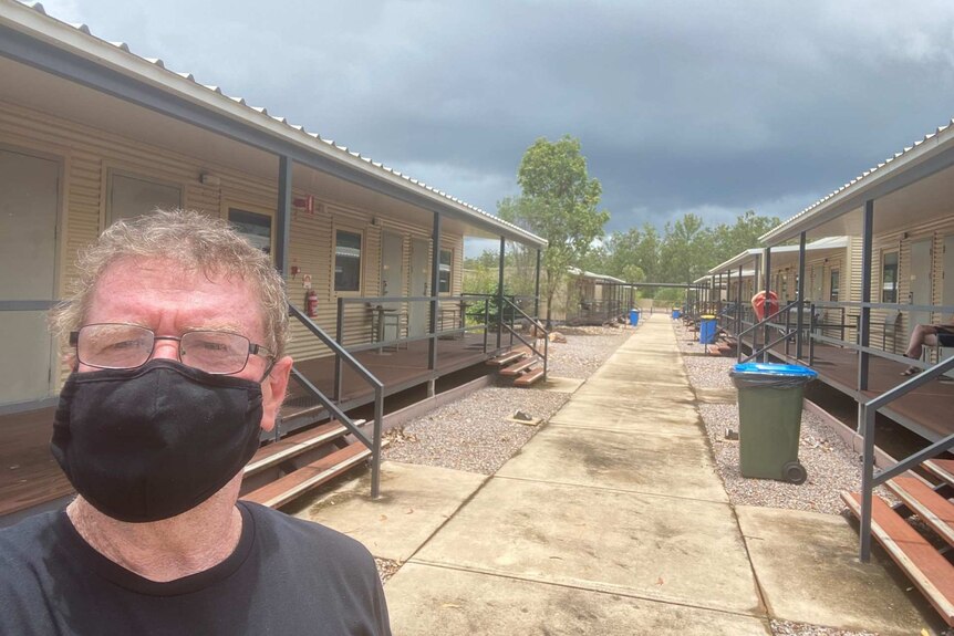An elderly gentleman wears a mask and stands inside a quarantine camp near Darwin.