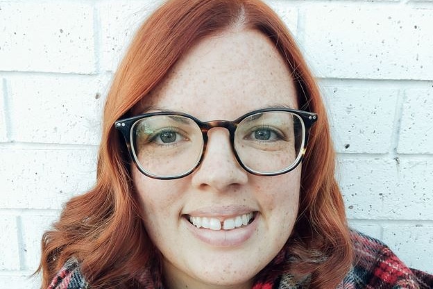 A young smiling woman wearing glasses and a tartan scarf.