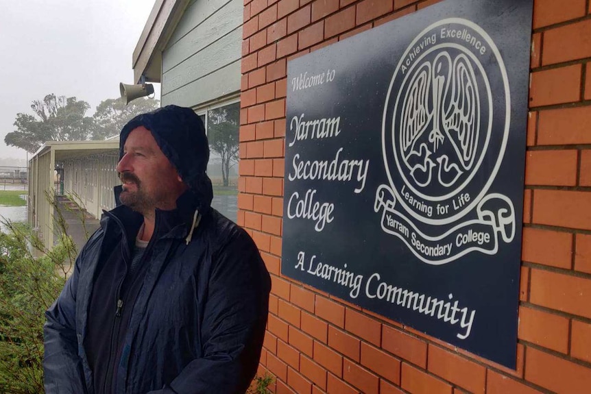 Yarram principal standing in front of school sign, flooding in background