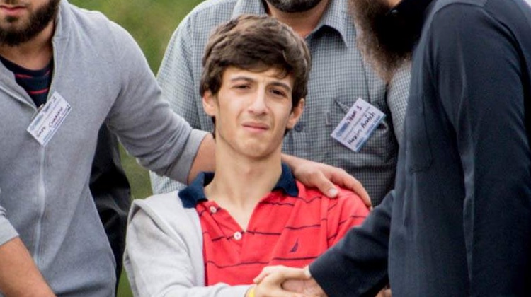 A boy in a wheelchair looking emotional while surrounded by people at his father and brother's funeral