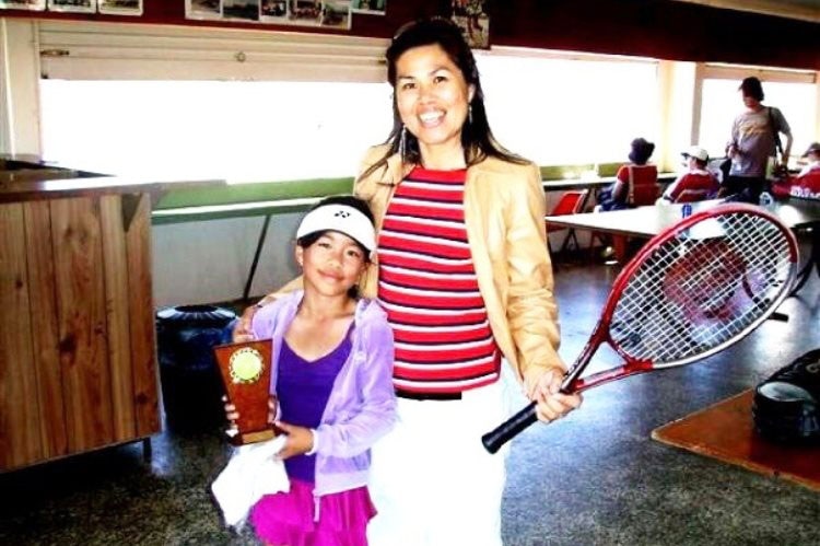Lizette Cabrera as a child, holding a trophy, with her mum holding a tennis racquet.