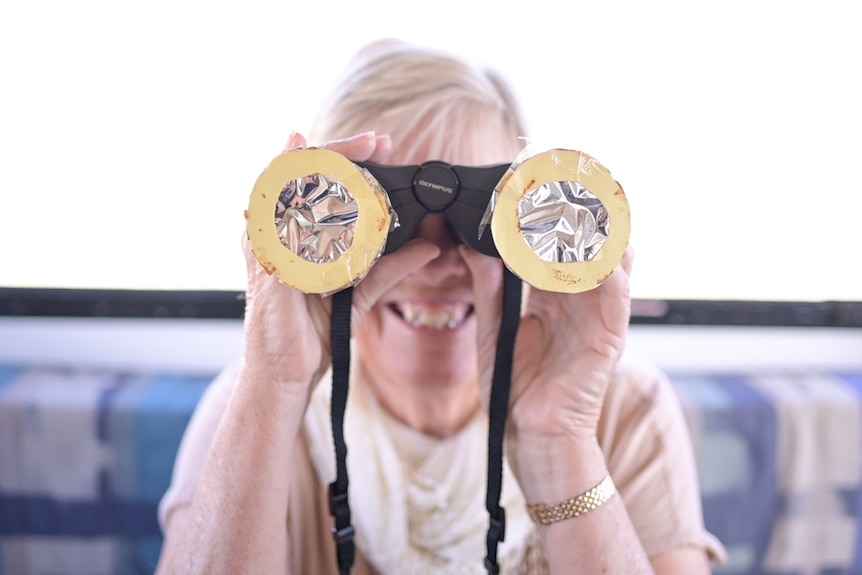 Portrait shot of a woman holding up foil-covered binoculars in front of her face.