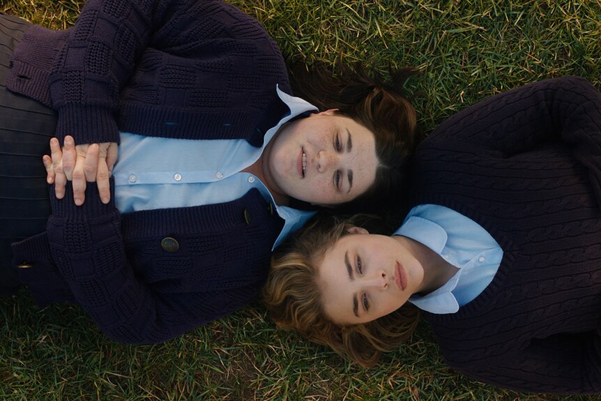 Melanie Ehrlich and Chloë Grace Moretz dressed in uniforms and lying flat on grass in film The Miseducation of Cameron Post.
