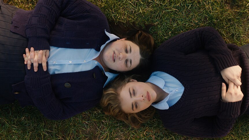 Melanie Ehrlich and Chloë Grace Moretz dressed in uniforms and lying flat on grass in film The Miseducation of Cameron Post.
