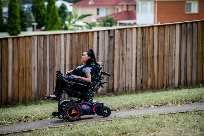 Melanie Tran goes downhill in her wheelchair, with a wooden fence in the background.