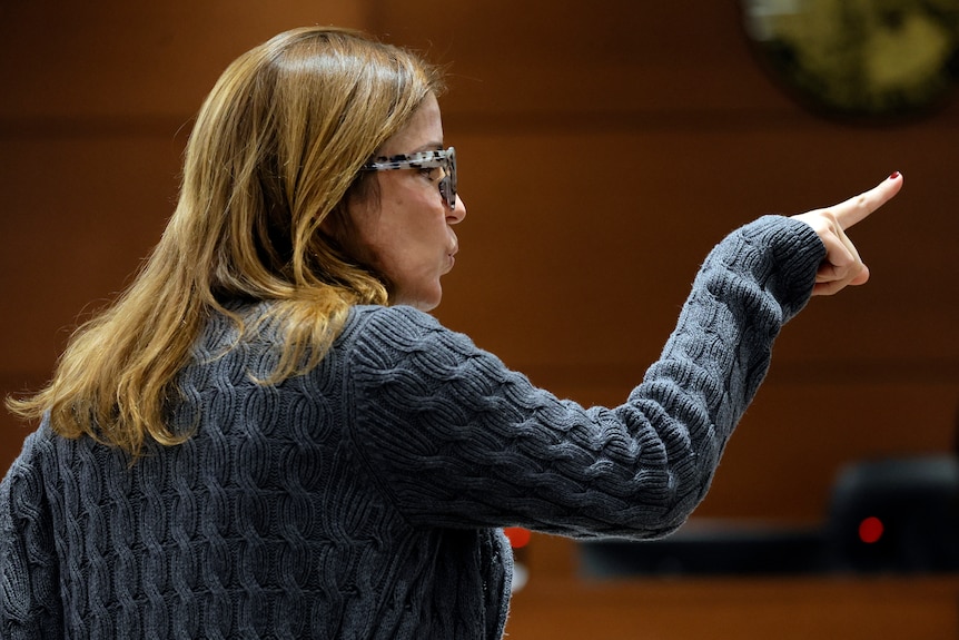 A woman points with her right hand as she delivers a victim impact statement in a courtroom.