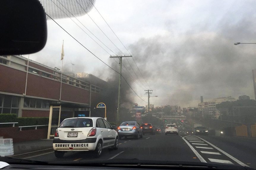 Image through a car windscreen of smoke billowing from the  XXXX brewery on Milton Road, at Milton and other traffic