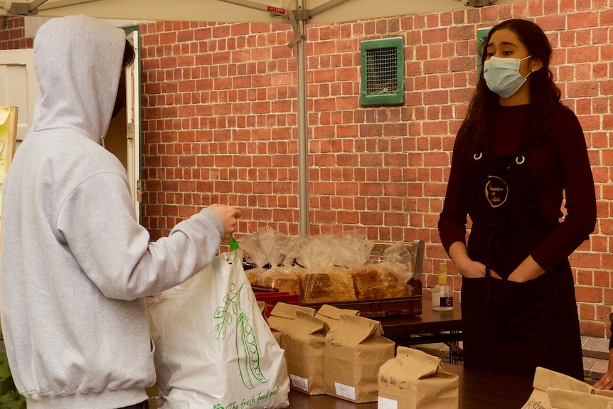 An international student in a hooded jumper receives a food package from the stall.
