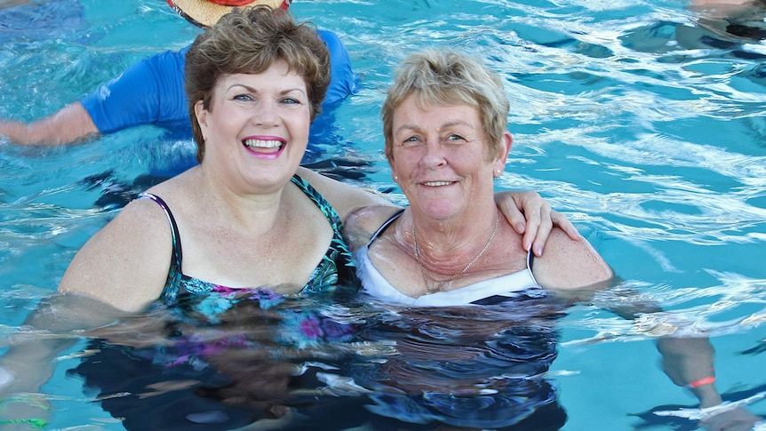 Two women hug in the pool during an aqua aerobics class