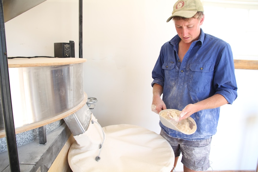 A man in blue shirt holds a fistful of flour.