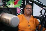 A woman sits at a radio desk in front of a microphone