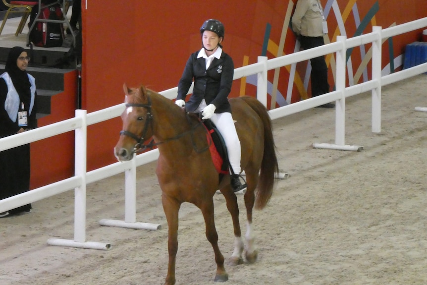 A girl is in formal dress on a horse competing in an arena in Abu Dhabi