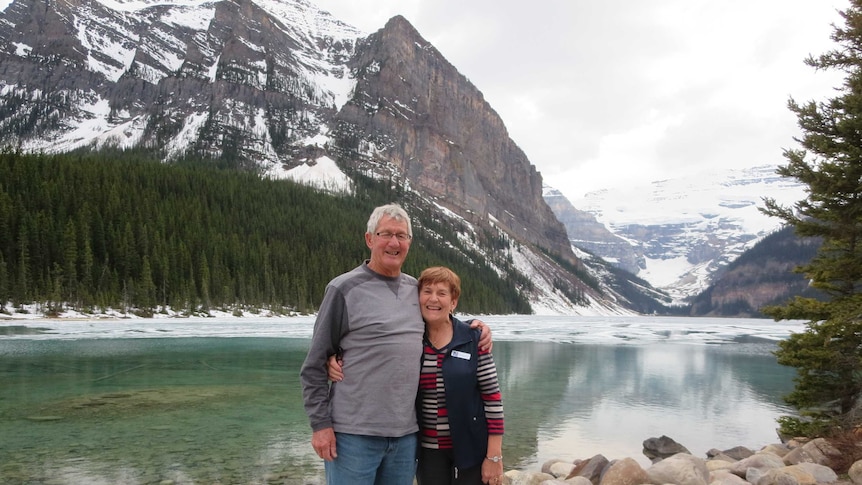 Man and woman in front of scenic mountain backdrop.