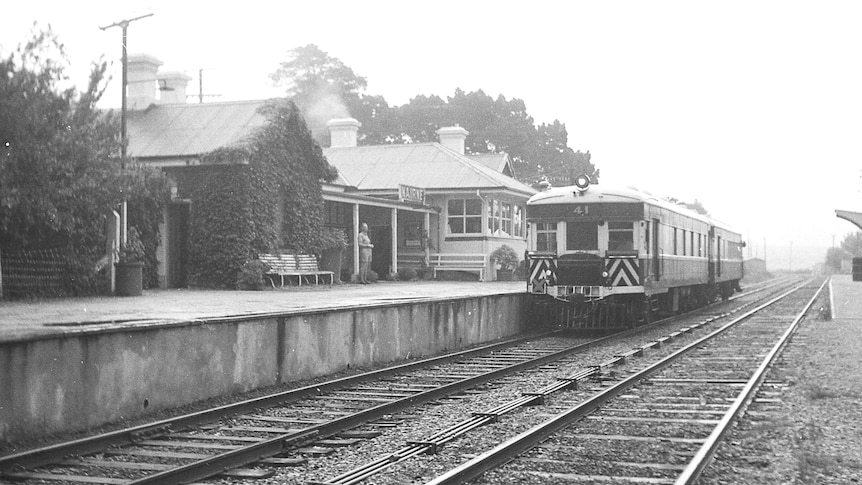 black and white image of train at Nairne train station with one man waiting on platform