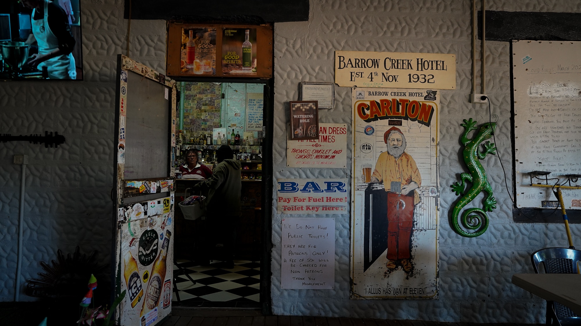 An open door leads into an outback pub, with signs reading 'WATERING HOLE' and 'BARROW CREEK HOTEL'.