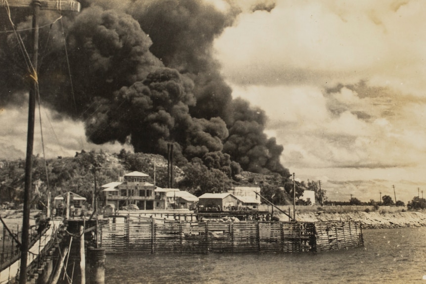 a monochrome image of smoke billowing out of oil tanks near the harbour
