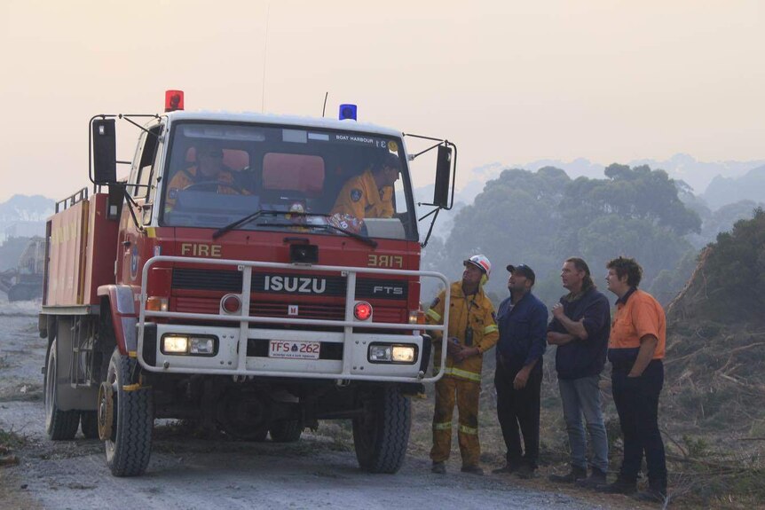 A group of men talk to a firefighter in a firetruck