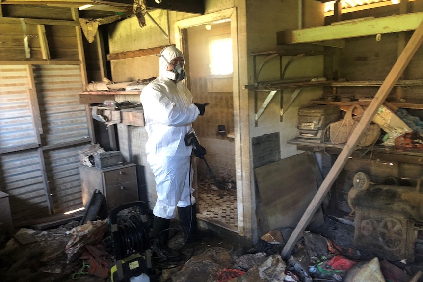 A man in a white hazmat suit inside a property covered in brown flood mud