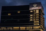 Tall buildings in the dark with lights on with an illuminated sign with the word Crown below a crown symbol.