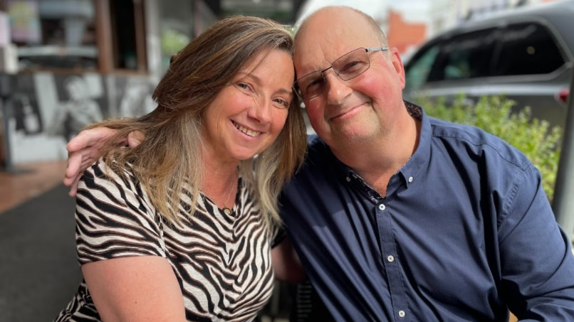 A woman and a man smiling and embracing sitting at a table.