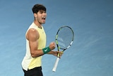 Male tennis player, yellow top, holding his racquet and pumping his fist, yelling in delight.