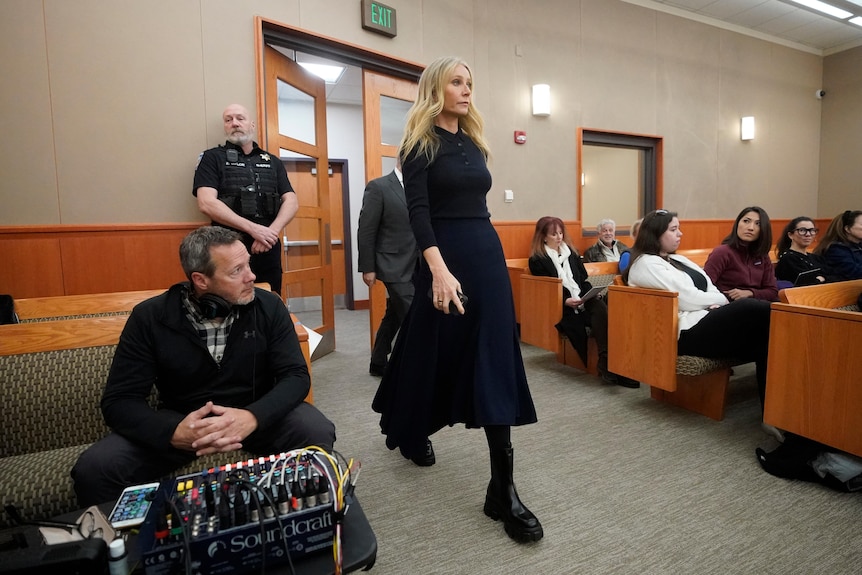 A blonde woman is pictured walking into a courtroom wearing black as people sitting on the benches look at her.