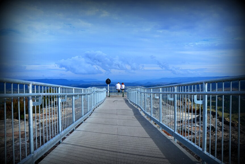 A picture looking down the walkway of a lookout with a very blue sky in the background and mountains