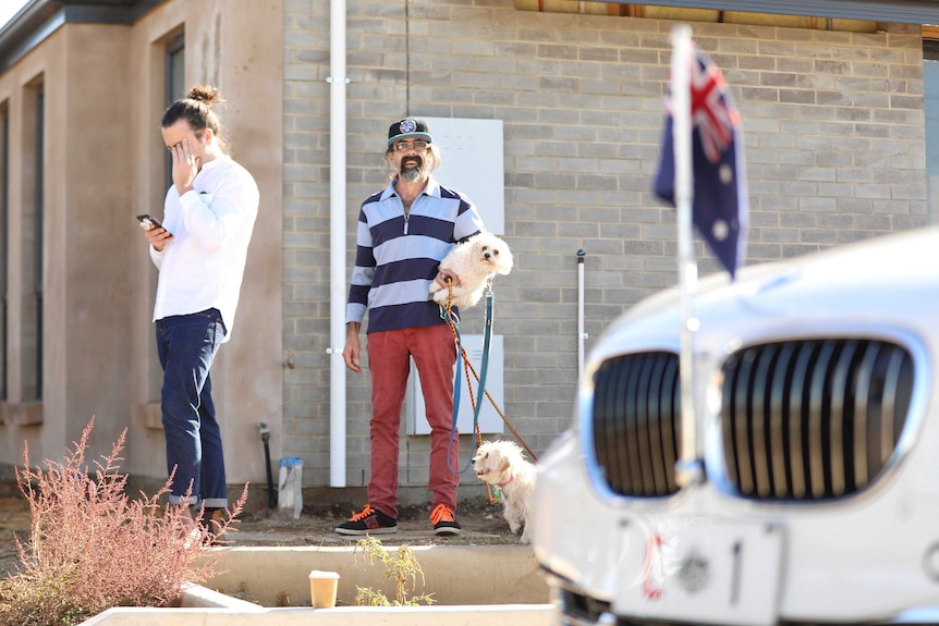 A man holds his dog as he looks towards the Prime Minister's car