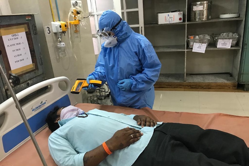 A female doctor in full protective gear treating a patient on a hospital bed