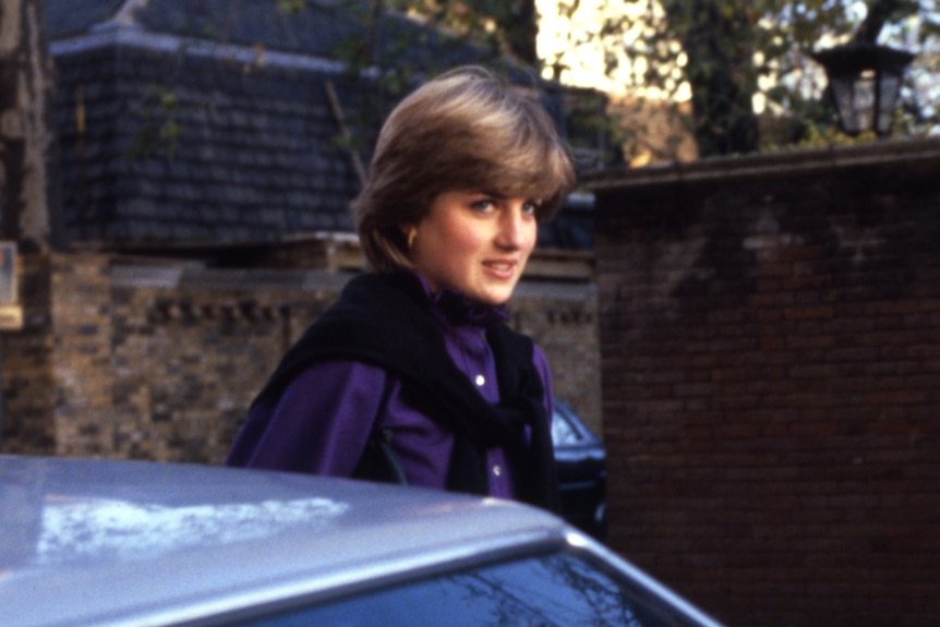 Diana Spencer smiles as she passes by a car wearing a scarf and blue shirt