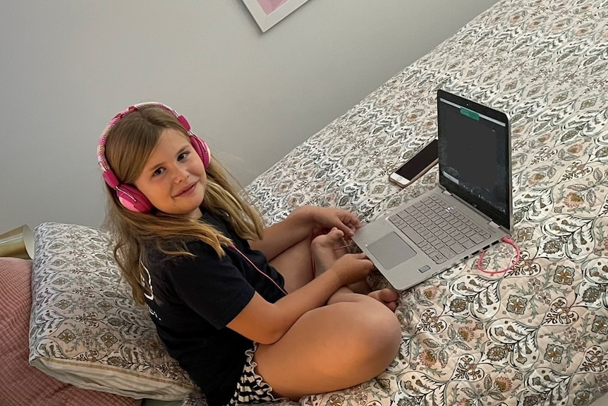 Young girl sits on a bed with her laptop.