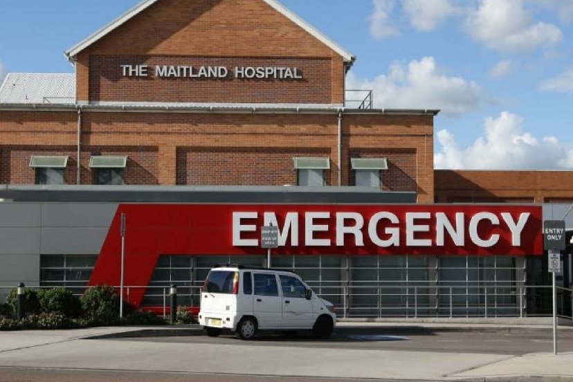 An old red brick building sits behind a modern hospital emergency sign.