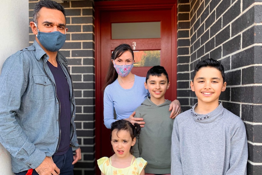 A family of five, comprising a man, woman, two boys and a girl, pose outside the front door of their home.