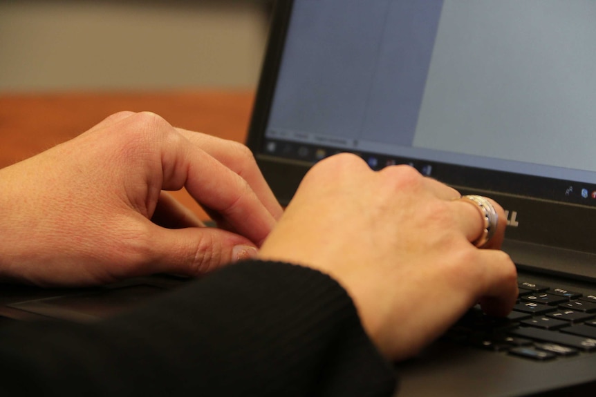 A woman's fingers types on a laptop keyboard