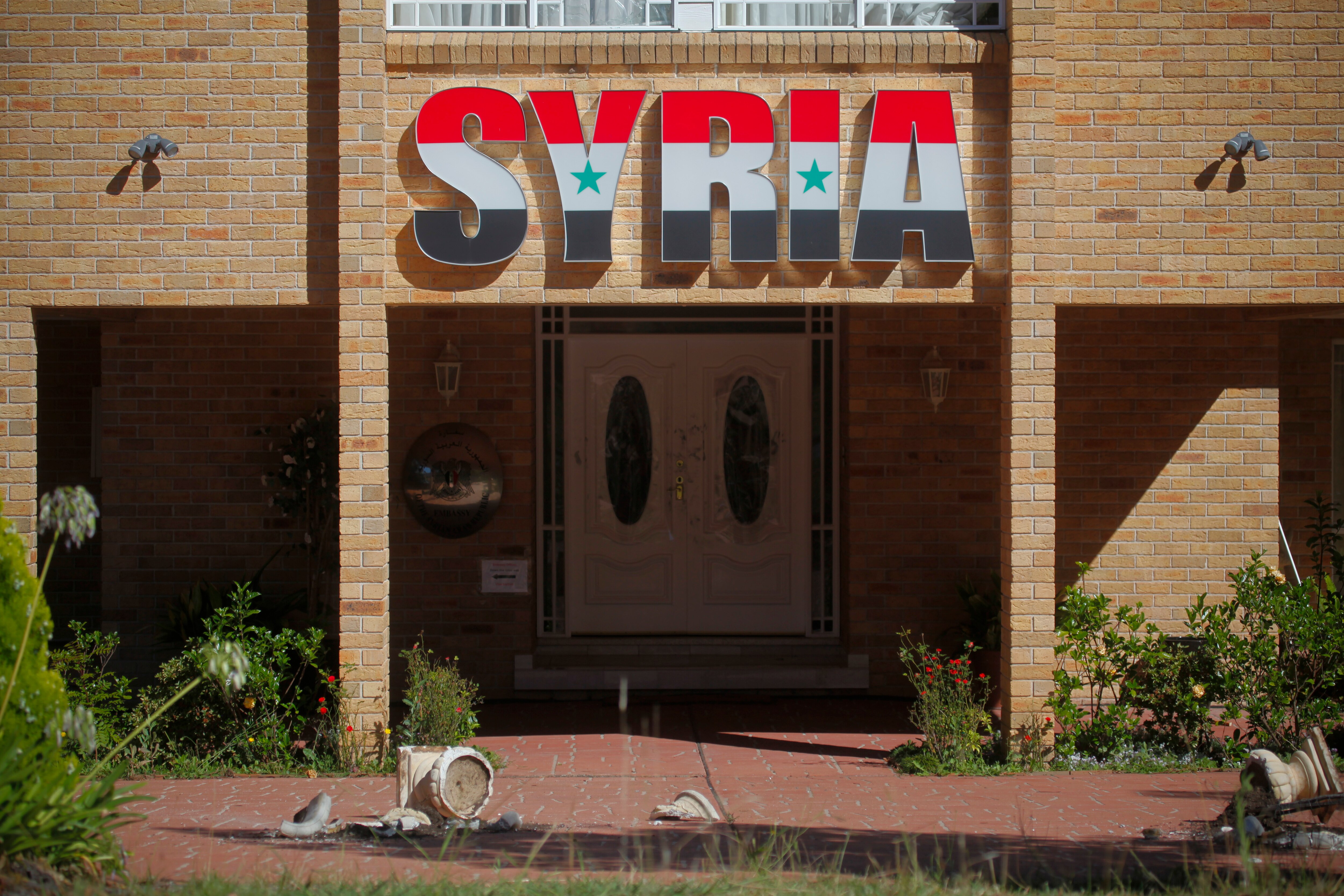 Broken windows and pot plants lie outside the Syrian Embassy in Canberra.