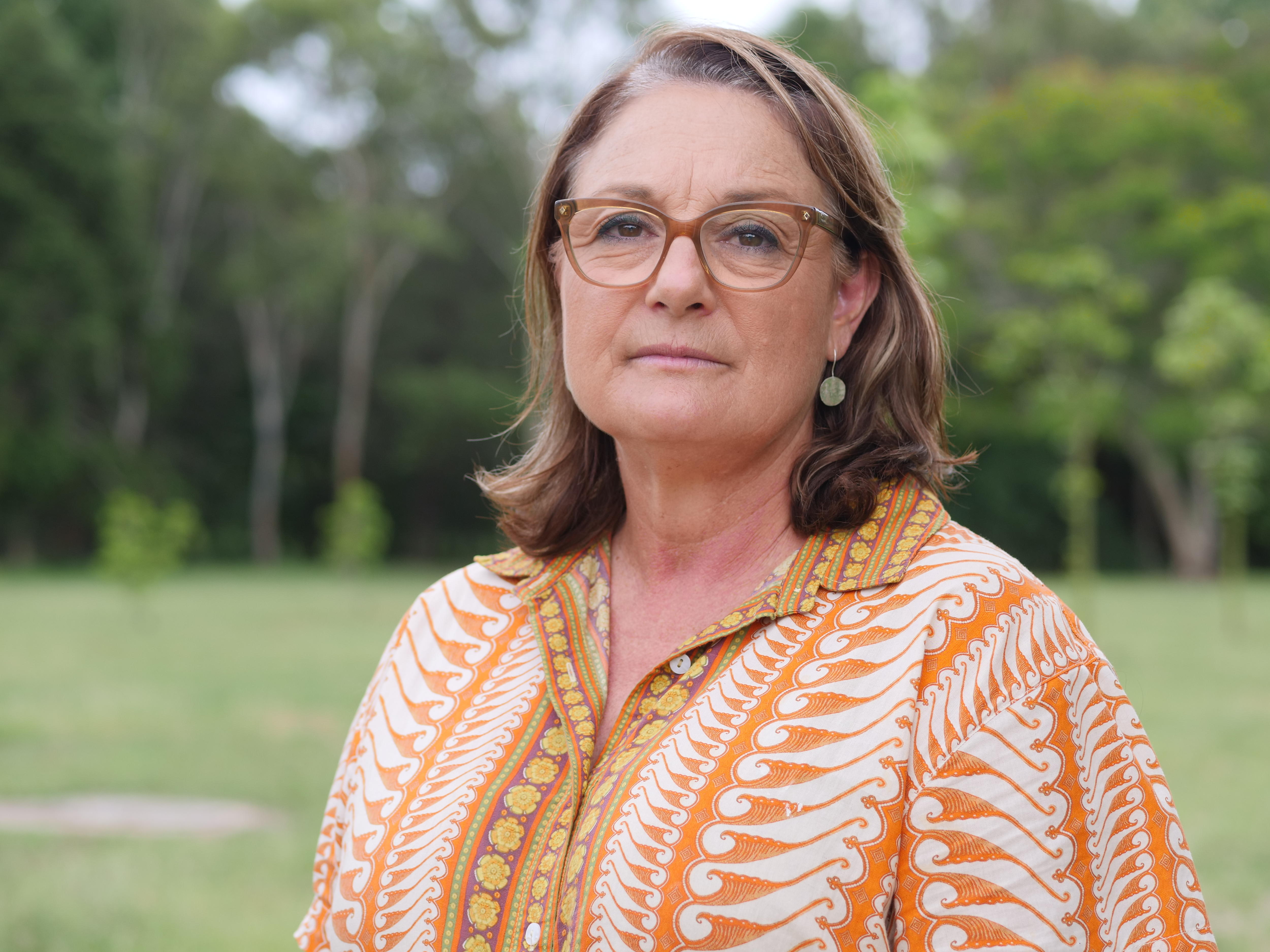 Uma mulher em frente a um parque verde, vestindo uma camisa laranja estampada e óculos