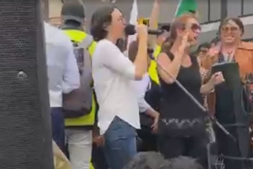 a woman in white with a microphone speaking to a crowd